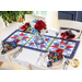 A red, white, and blue table runner made with floral fabrics laid flat on a white table next to cloth napkins