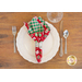 Single red napkin with green plaid on the inside in a ring and fanned out on a white plate with place setting atop a wood table