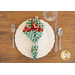 Single green plaid napkin with red christmas pattern on the inside in a ring and fanned out on a white plate with place setting atop a wood table