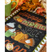 A fabric wall hanging with autumn themed words, pumpkins, and cups of coffee laid flat on a table