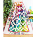 A colorful quilt with geometric patterns and floral designs draped over a display, surrounded by greenery.