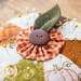 An orange, white, and green pin cushion with a small button topper on a wood table