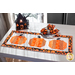Table runner featuring 3 pumpkins made of strips of orange and black halloween themed fabrics on a table set with a plate and matching napkins.