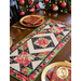 Photo of the Madison table runner made with Christmas fabrics with gold accents on a wooden table with four place settings with matching napkins and a decorated Christmas tree on one side.