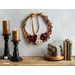 Wreath of foliage and flowers toped with a gold ribbon hanging from wall next to books and candles.