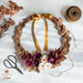 Wreath of foliage and flowers toped with a gold ribbon resting on a table top.