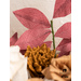 Close up of gold and white paper flowers and red paper leaves with stems in a clay vase.