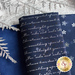 Close up of navy blue fabric with metallic silver winter motifs layered atop one another on a white counter with silver ferns laying across them