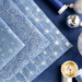 Array of folded light blue fabrics with metallic silver swirls and stars/burst patterns with spools of blue and silver thread next to it with silver baubles on a dark blue countertop