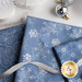 Array of folded light blue fabrics with metallic silver swirls and stars/burst patterns with silver baubles and tree decorations next to it on a white countertop
