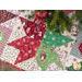 Tree skirt with patchwork and geometric star design made of red, white, and green, Christmas themed fabrics.