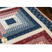 Table runner with four blocks of rectangular strips of fabric, featuring cream, read, and blue patriotic prints.