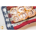 An close-up image of an Americana Casserole Hot Pad with a casserole dish of cinnamon rolls on a white table..