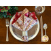 A festive table setting with a plate, fork, knife, and elegantly folded patterned napkins in red and gold.