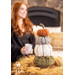 4 Flannel pumpkins stacked on top of each other resting on a table with a woman with a coffee cup in the background.