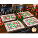 Set of 4 christmas placemats on a brown and black table with black chairs and Christmas decorations in the background and a wreath in the center with a gingerbread man decoration