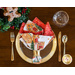 Single napkin in a gold napkin ring sitting on a gold place setting with a wreath and gingerbread man decoration