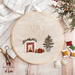 A circular hand embroidery project with the word Joy and a small fireplace with Christmas presents