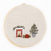 A circular hand embroidery project with the word Joy and a small fireplace with Christmas presents on a white background