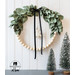 Vintage winter wreath with green felt leaves, wooden beads and a black velvet ribbon hanging on a white paneled wall with mini evergreen tree decorations on a tabletop in the foreground