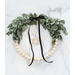 Vintage Winter Hoop Wreath lying on a white marble surface with pale wooden beads, green felt leaf decoration, a black velvet ribbon tied in a bow, and a small wooden snowflake.