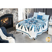 Bedroom scene with Ice Castles quilt draped over a bed in front of a rustic stone fireplace with a white tree in the background and dark blue armchair in the foreground