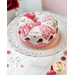 Love pinwheel pastry pin cushion on a decorated white cake stand with red roses in the background, all on a white tabletop with pink buttons and thread
