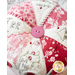 Close up of center of pin cushion with a large pink button and pink and red fabrics alternating with cream wedges in a pinwheel