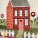 close up image of full quilted house made with red, blue-gray, and pink floral fabrics with yo-yo flowers with buttons and a white picket fence.