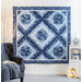 a blue and white quilt hanging on a white wall with a dark chair in the foreground and a small white shelf with winter decorations