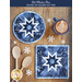 Top down image of two blue hot pads made with the Blizzard Blues collection on a brown wooden table with a cup of hot cocoa, two wooden spoons, and snowflake decorations scattered all over.