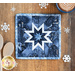 Square blue hot pad with a white star in the center on a brown table with a cup of hot cocoa and wooden spoons with snowflake decorations.