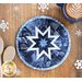 Round blue hot pad with a white star in the center on a brown table with a cup of hot cocoa and wooden spoons with snowflake decorations.