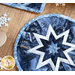 Round blue hot pad with a white star in the center on a brown table with a wooden spoon and snowflake decorations.