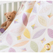 Close up of draped quilt in a white crib with a stuffed bear with purple feet in the background