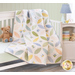 Orange Blossom Little Lambies Spring quilt draped over a white crib with a stuffed bear sitting next to it on the mattress and a shelf with a lamp and stack of fabric from the Little Lambies Flannel collection in the background