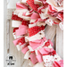 Close up of top corner of fabric wreath showing detail of red, pink, and white fabrics on a white wooden wall