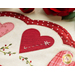 close up of scalloped edge showing embroidery detail of a small white arrow on a red heart with  stitched green leafy vines below it