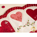 angled close up of scalloped edge showing embroidery detail of a small white arrow on a red heart with  stitched green leafy vines below it