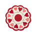 Isolated image on a white background of a round white table topper with scalloped edges and red and pink hearts in a circle around it, on a white countertop with red buttons, red thread, red roses, and scissors with a plant in the background
