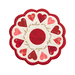 Isolated image on a white background of a round white table topper with scalloped edges and red and pink hearts in a circle around it, on a white countertop with red buttons, red thread, red roses, and scissors with a plant in the background