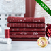 Stack of 6 folded dark red fabrics with metallic silver snowflakes, script, and stars/burst patterns with spools of red and silver thread and a large red bauble next to it on a white countertop with a pale room in the background and a green banner in one corner that reads: 