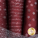 Close up of dark red fabric with metallic silver winter motifs and script patterns layered atop one another with a mesh silver ribbon laying on top