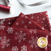 Close up of dark red fabric with metallic silver winter motifs layered atop one another on a white countertop with red and silver spools of thread and a silver ribbon laying next to them