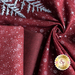 Close up of dark red fabric with metallic silver winter motifs patterns layered atop one another with a silver fern laying on top of a gathered fabric in a swirl