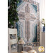 Angled shot of farmhouse cross quilt in cream and teal colors with a house plant and small white chair with home decor items on it in the foreground
