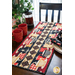 coffee-themed table runner with a checkered stripe and coffee mugs in neutral tones, red, and black on a brown dining table with a window and house plant in the background and red mugs, french press, and plates with matching napkins on the sides.