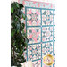 A patchwork quilt with classic quilt star blocks in soft blue, pink, and cream hanging on a white paneled wall with a dark green houseplant in the foreground