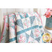 A patchwork quilt with classic quilt star blocks in soft blue, pink, and cream draped over furniture leaning against a white paneled wall with a small white shelf and pink flowers in a can in the background