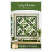Front cover of Lucky Charms Wall Hanging pattern featuring Small quilt wall hanging featuring pieced shamrocks with geometric designs all in green and cream. A potted plant, green house tree, and a green mug atop a small stack of fabric from the Lucky Charms 